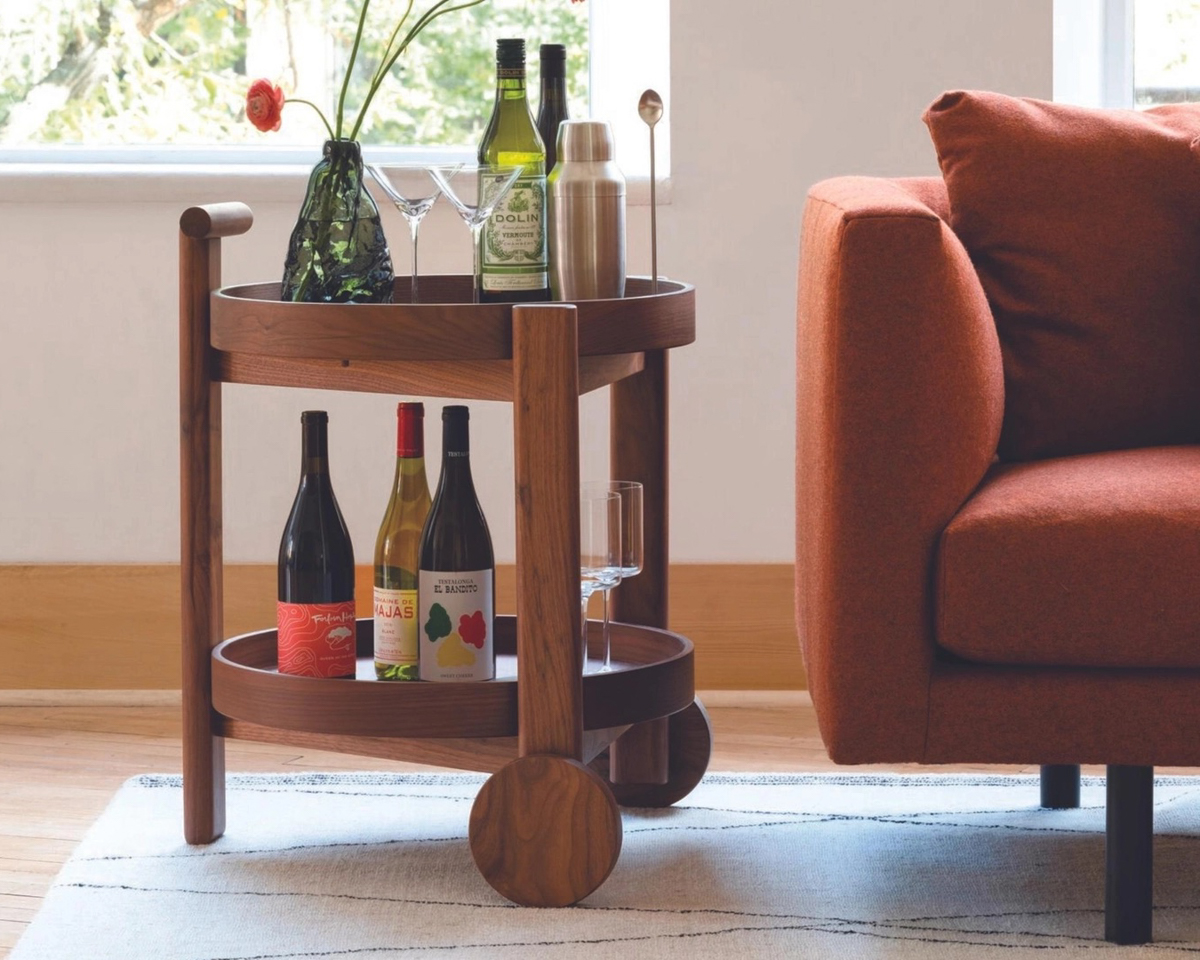 Bart Cart by EQ3 in walnut wood finish with bottles and glasses with a vase and flower next to a red orange sofa